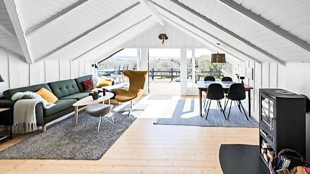 A spacious loft with a high ceiling, a dining area with a table and chairs, a sofa with cushions, and a television.