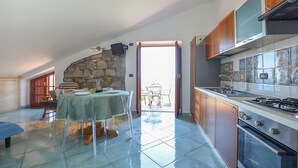 A kitchen with a stone wall, a dining area with a table and chairs, and a view through an open door.