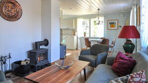 A cozy living room with a wooden table, a sofa, and a fireplace. There is a kitchen in the background with a dining area. - 2 bEdroom gorgeous home in Ed (Ed)