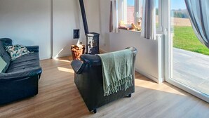 Un saló modern amb un sofà negre, una manta verda i una finestra gran amb vista a un camp verd.