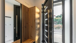 A modern hallway with a wooden bench, a black door, and a view of a garden outside.