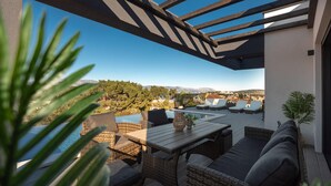 A covered outdoor seating area with wicker furniture, a pool, and a view of a mountainous landscape.