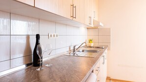 Een moderne keuken met lichte houten kastjes, witte metrotegels, een marmeren aanrechtblad, roestvrijstalen apparatuur en een kleine vaas met bloemen op de gootsteen.