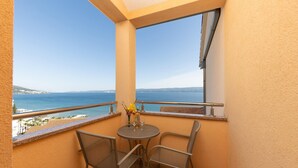 Een balkon met uitzicht op zee, een tafeltje met stoelen en een vaas met bloemen.
