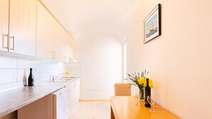 Een moderne keuken met witte kastjes, een houten aanrecht en een eethoek met een houten tafel en stoelen. Er hangt een lijst aan de muur en op de tafel staat een vaas met bloemen.