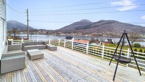 A wooden deck with wicker furniture, a swing, and a view of a river and mountains. - Amazing home in Nedre Vats with house sea view (Nedre Vats)