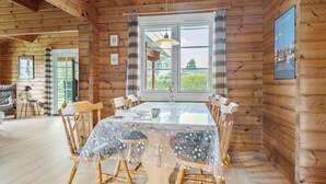 A wooden cabin interior with a dining table, chairs, and a large window.