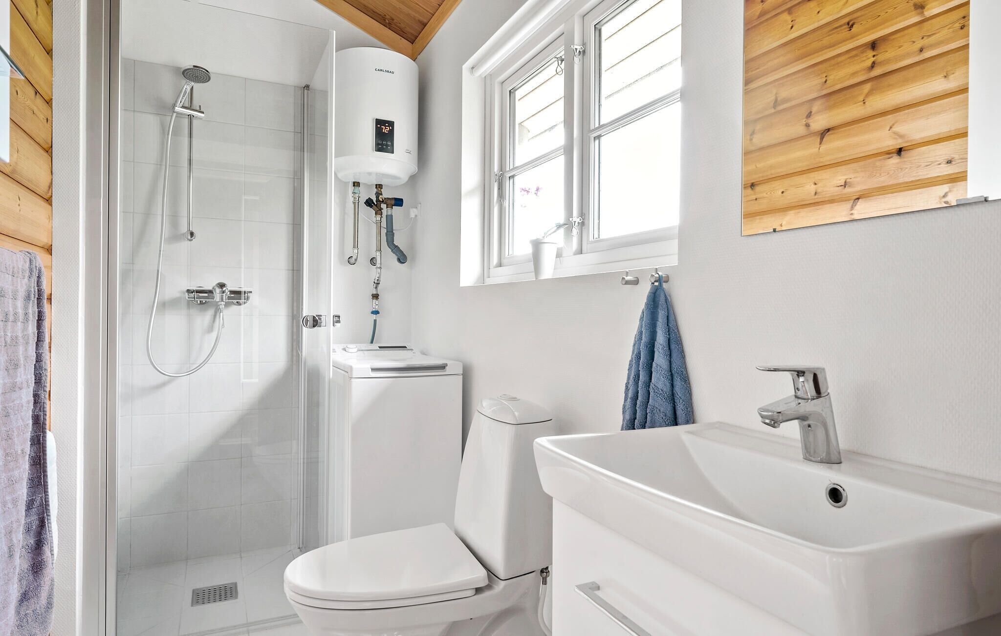 Une salle de bain moderne avec une douche à parois de verre, des toilettes blanches et un lavabo sous un plafond en bois.