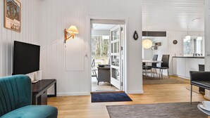 A modern living room with a television, a teal sofa, a dining area with a table and chairs, and a kitchen visible through an open door. - Awesome home in Nexø with sauna (Nexø)
