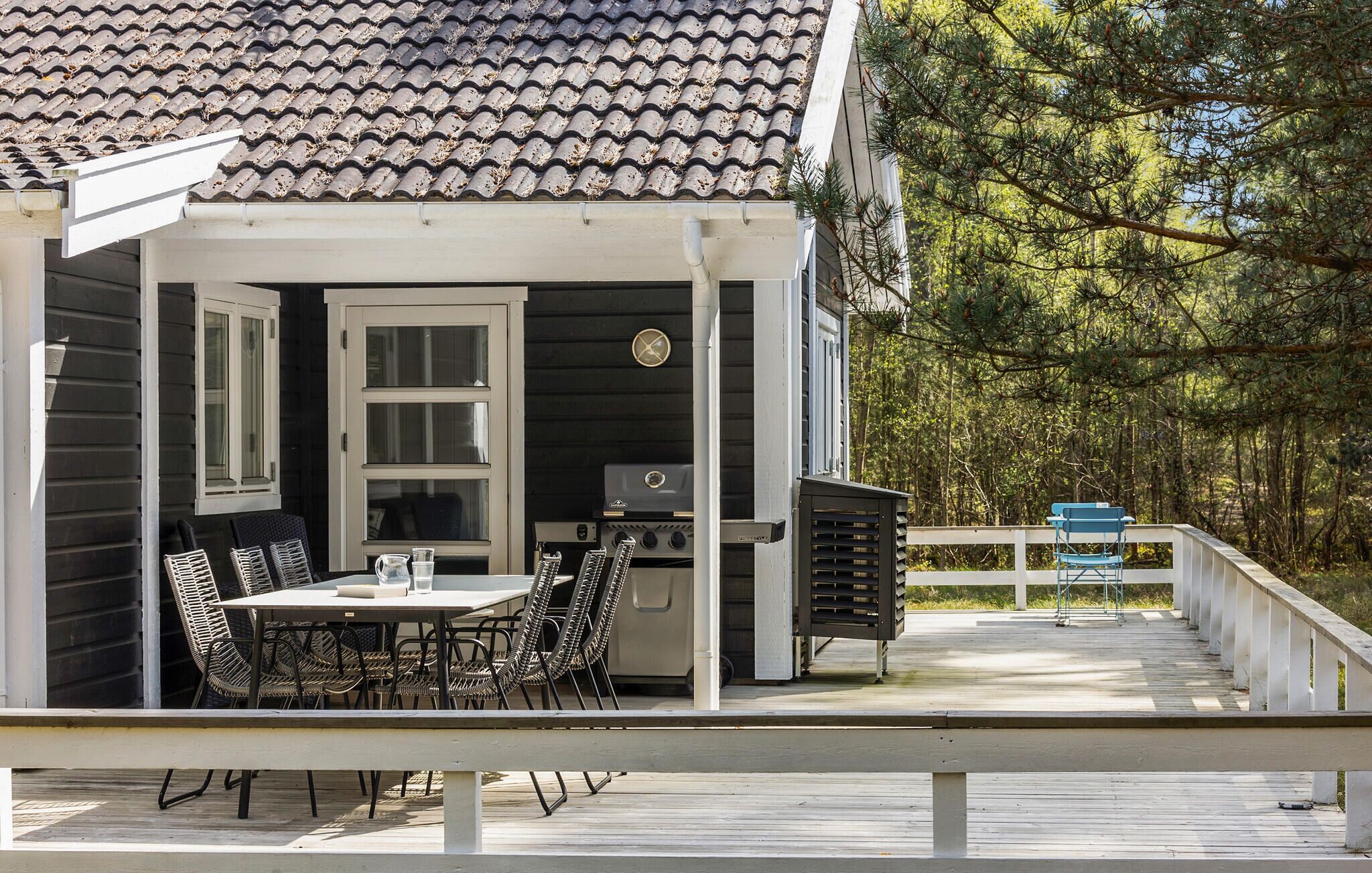 Un espacio exterior techado con comedor, que incluye una mesa, sillas, una parrilla y vistas a un bosque.