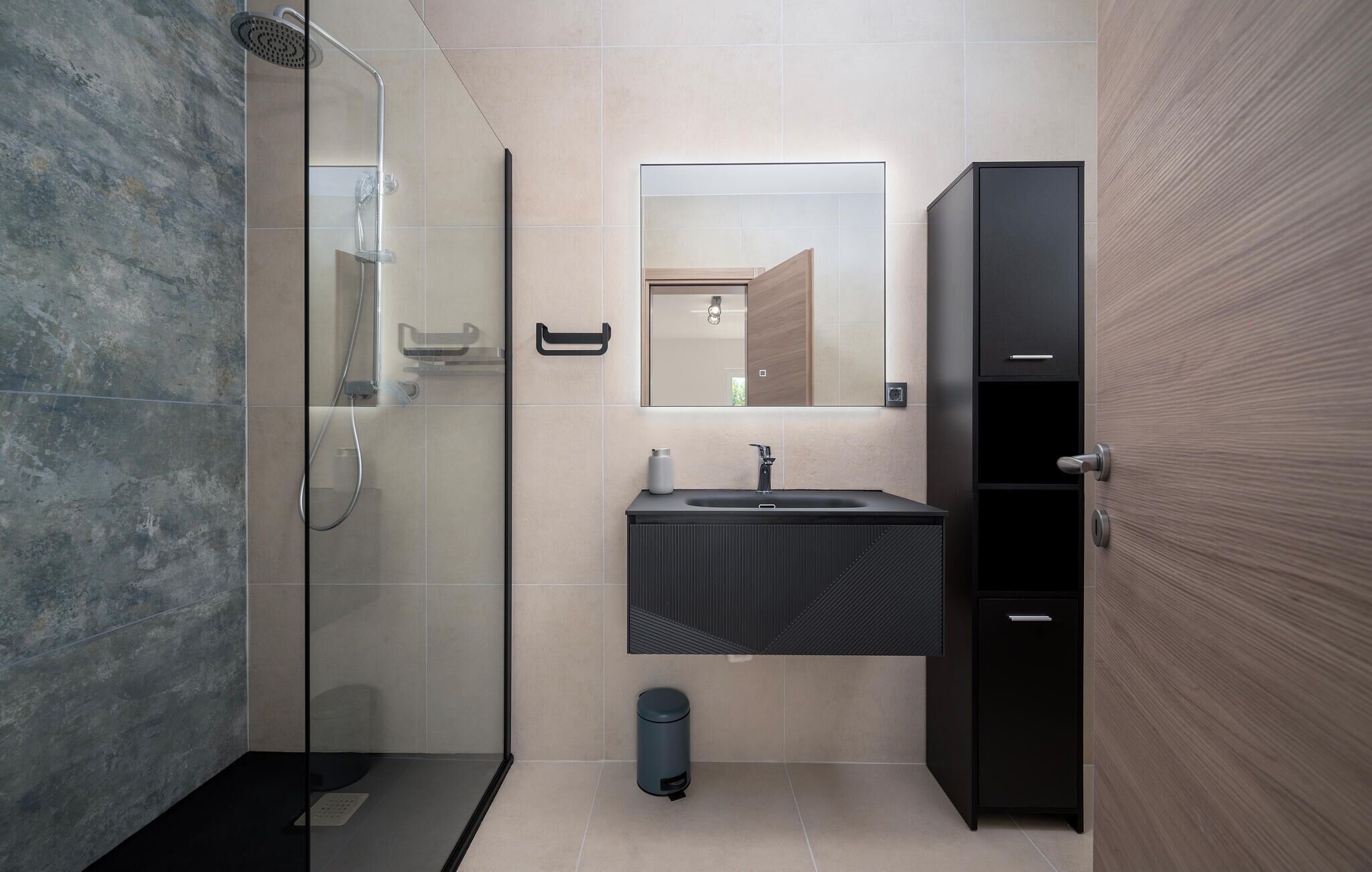 Un baño moderno con ducha envuelta en vidrio, un lavamanos con espejo y un mueble negro.