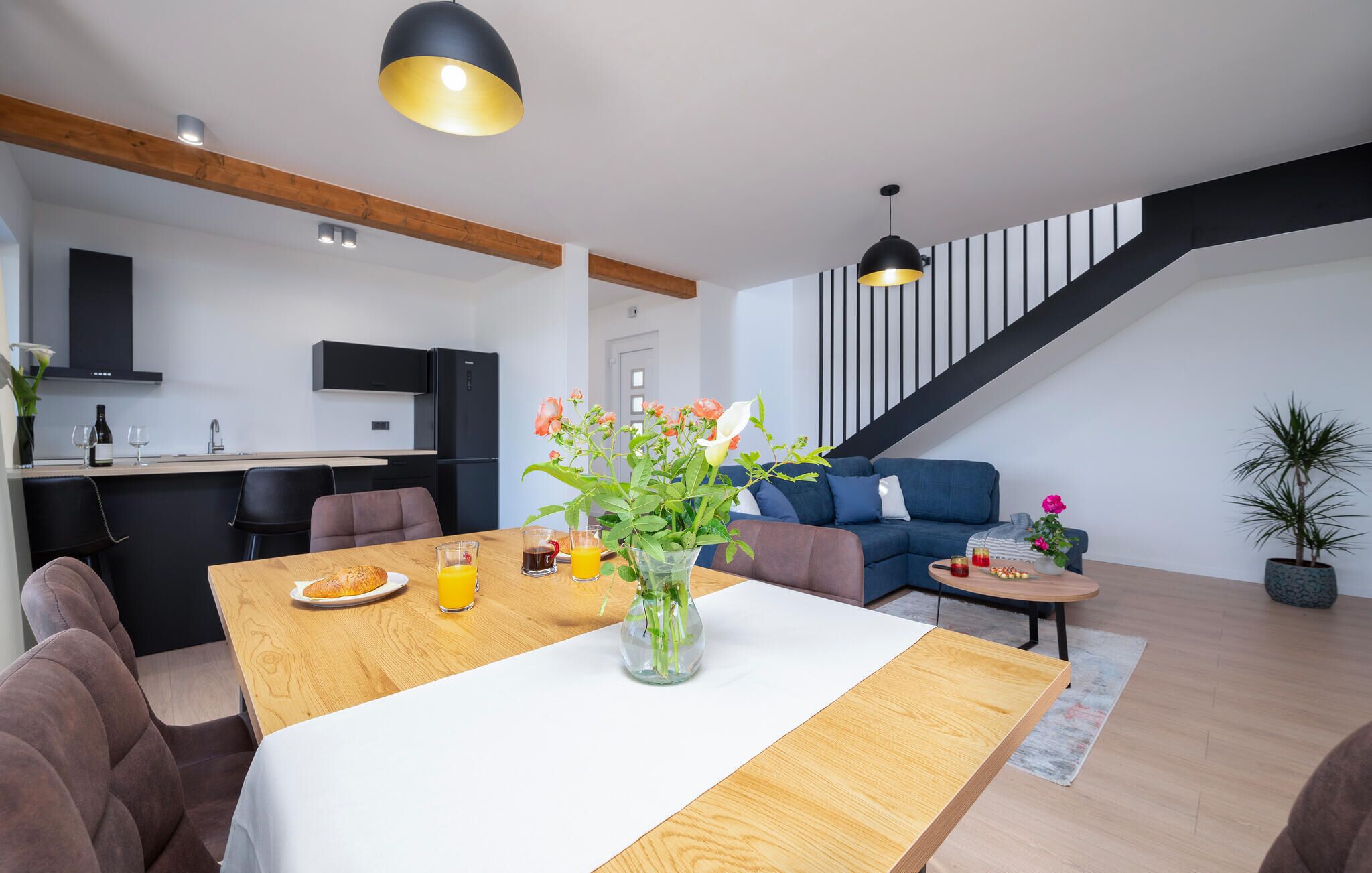 A modern living space with a dining area, kitchen, and staircase.
