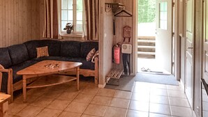 A cozy living room with a dark-colored sofa, a wooden coffee table, and a tiled floor. There is a window with curtains, a small table with a vase, and a fire extinguisher mounted on the wall. - Nice apartment in Sälen with sauna (Sälen)