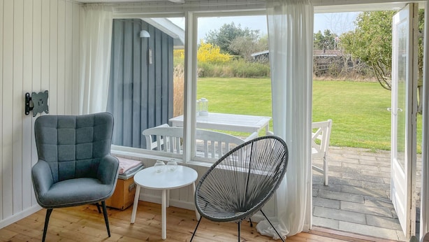 A conservatory with a grey upholstered chair, a wicker chair, and a small round table. - 2 bedroom lovely home in Dannemare (Dannemare)
