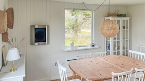 A dining area with a wooden table and white chairs, a white cabinet with glass doors, and a window with a view of trees and grass. - 2 bedroom lovely home in Dannemare (Dannemare)