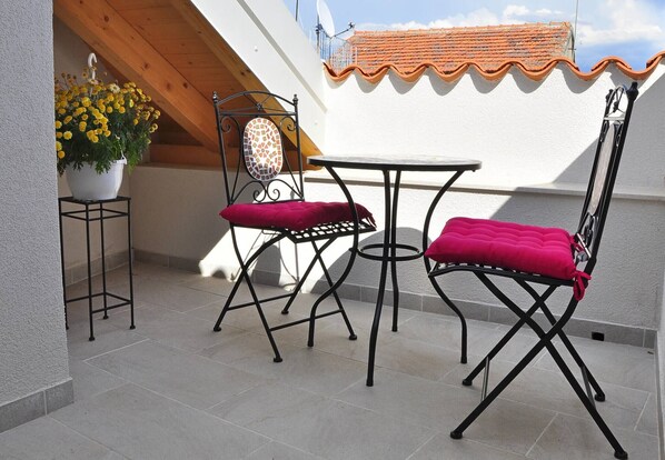 A small outdoor patio with a white table and two chairs, a potted plant with yellow flowers, and a tiled roof. - Room-room With the City and sea View (Split)
