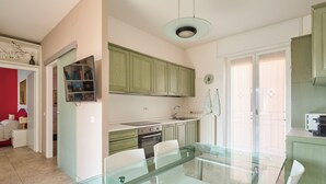 A modern kitchen with green cabinets, a glass dining table, and white chairs.