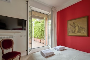 Une chambre d’hôtel avec un lit, une chaise, un téléviseur, un tableau et une vue sur la verdure par une porte ouverte.
