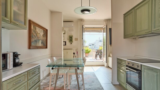 A modern kitchen with a glass dining table, green cabinets, and a view to the outside.