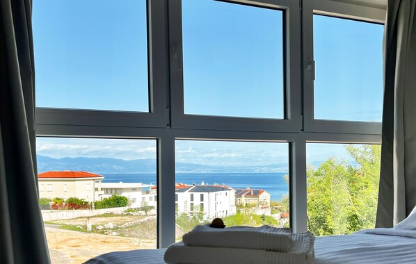Une chambre dotée d’une grande fenêtre donnant sur la mer et les bâtiments environnants.