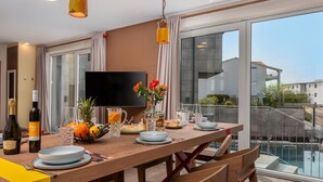 A modern dining area with a wooden table set for a meal, a TV, and a view of a residential area.