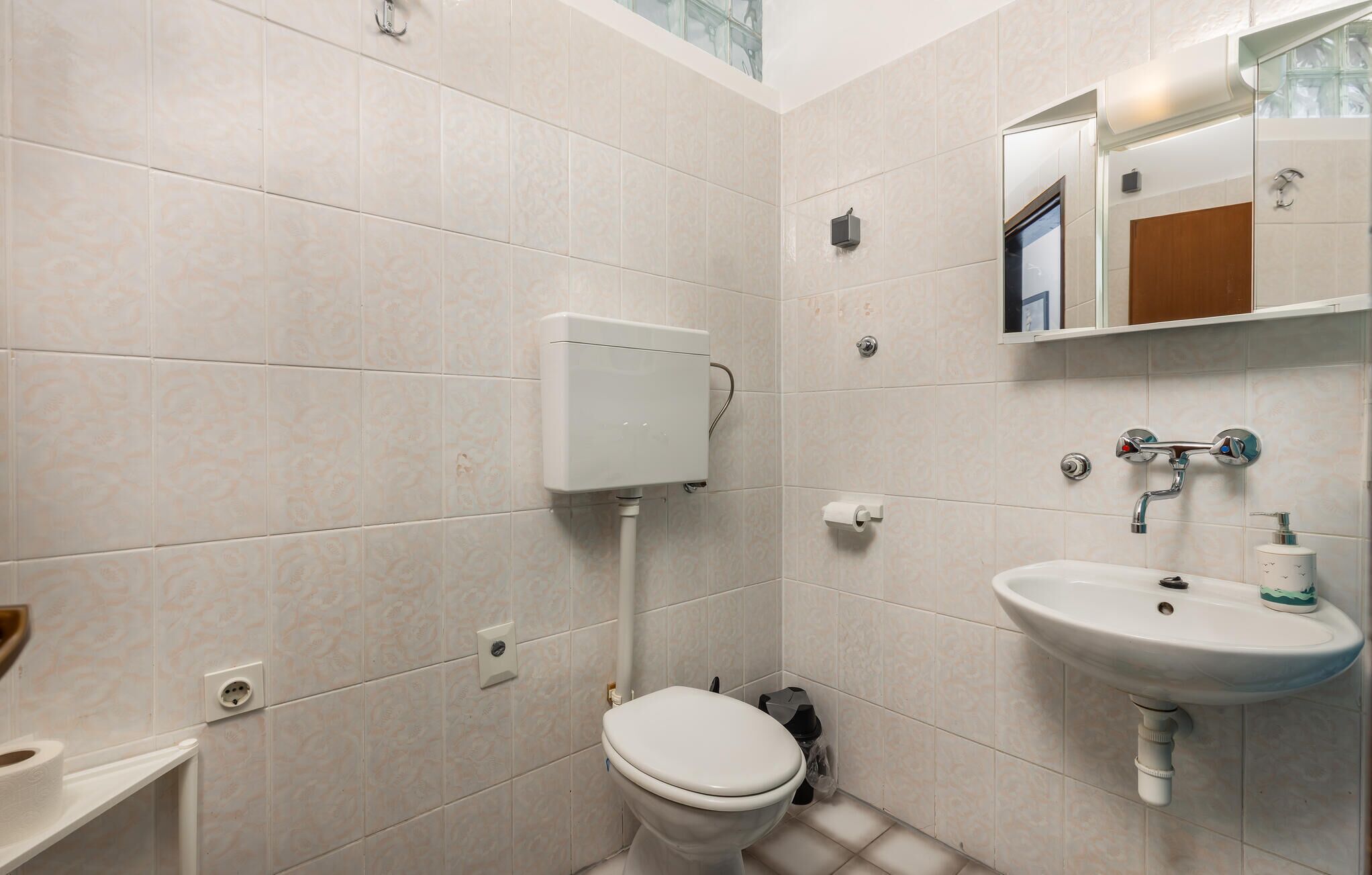 Et lille badeværelse med toilet, håndvask og toiletpapirholder.