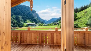 Een houten terras met uitzicht op een bergachtig landschap, inclusief een huis en een vallei.