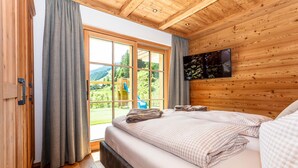 Een slaapkamer met een groot raam, houten plafond en een bed met geruit beddengoed.