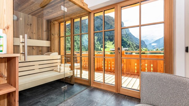 Een sauna met een houten bank, grote ramen en uitzicht op een bergachtig landschap.