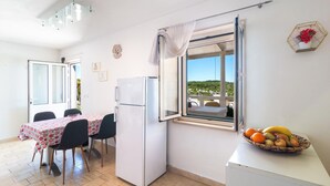 A compact kitchen with a refrigerator, a dining table with chairs, and a window with a view of greenery.