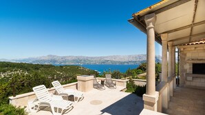 A terrace with lounge chairs overlooking a scenic view of the sea and mountains.