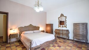 A bedroom with a large bed, a chandelier, a dresser, a mirror, and a nightstand with a lamp.