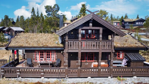 A wooden chalet with a thatched roof, a balcony, and a covered outdoor seating area.