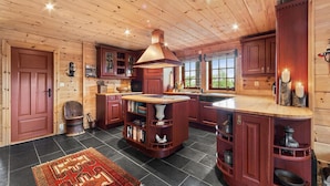 A wooden cabin interior with a central island, built-in bookshelves, and a large window providing natural light.
