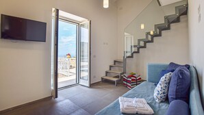 A modern living room with a sofa, a TV mounted on the wall, a staircase, and a view through an open door. - Amazing home in Castellabate with WiFi (Castellabate)