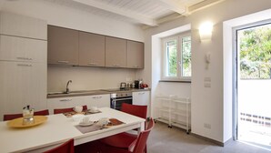 A compact kitchen with white cabinets, a dining table with red chairs, and a window providing natural light. - Amazing home in Castellabate with WiFi (Castellabate)