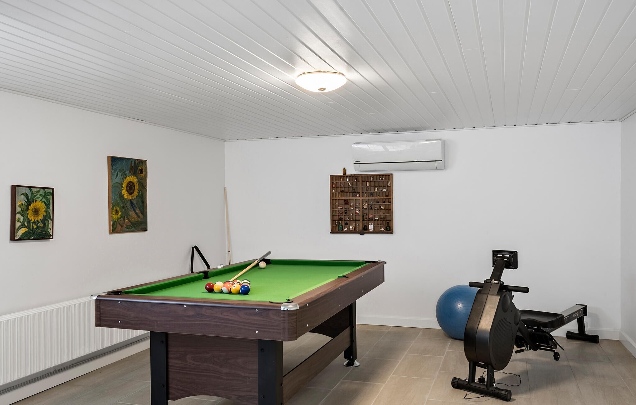 Quarto com mesa de bilhar, equipamentos de ginástica e ar condicionado fixado na parede.