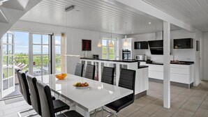 A modern kitchen with white cabinetry, a dining area with a white table, and a large window overlooking greenery. - Stunning home in Fjerritslev with sauna (Fjerritslev)