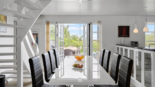 A modern dining area with a white table, black chairs, and a bowl of fruit. - Stunning home in Fjerritslev with sauna (Fjerritslev)