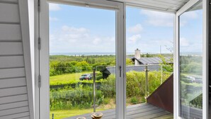 A balcony with a glass door leading to a view of a green landscape and a distant building. - Stunning home in Fjerritslev with sauna (Fjerritslev)