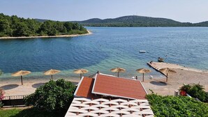 A beach with clear water, umbrellas, and a building with a red roof. - Awesome apartment in Pirovac with WiFi (Pirovac)