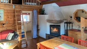 A cozy cabin interior with a wooden interior, a loft bedroom, a fireplace, and a dining area.