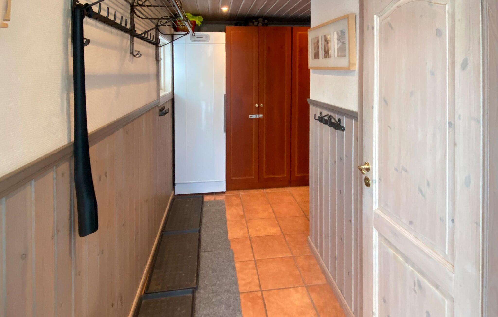 A narrow hallway with a wooden door on the right, a white door in the center, and a metal rack on the left.