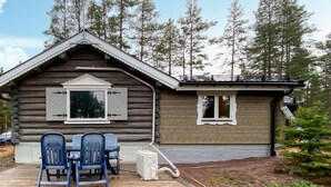 A log cabin with a deck, two chairs, and a small heater.