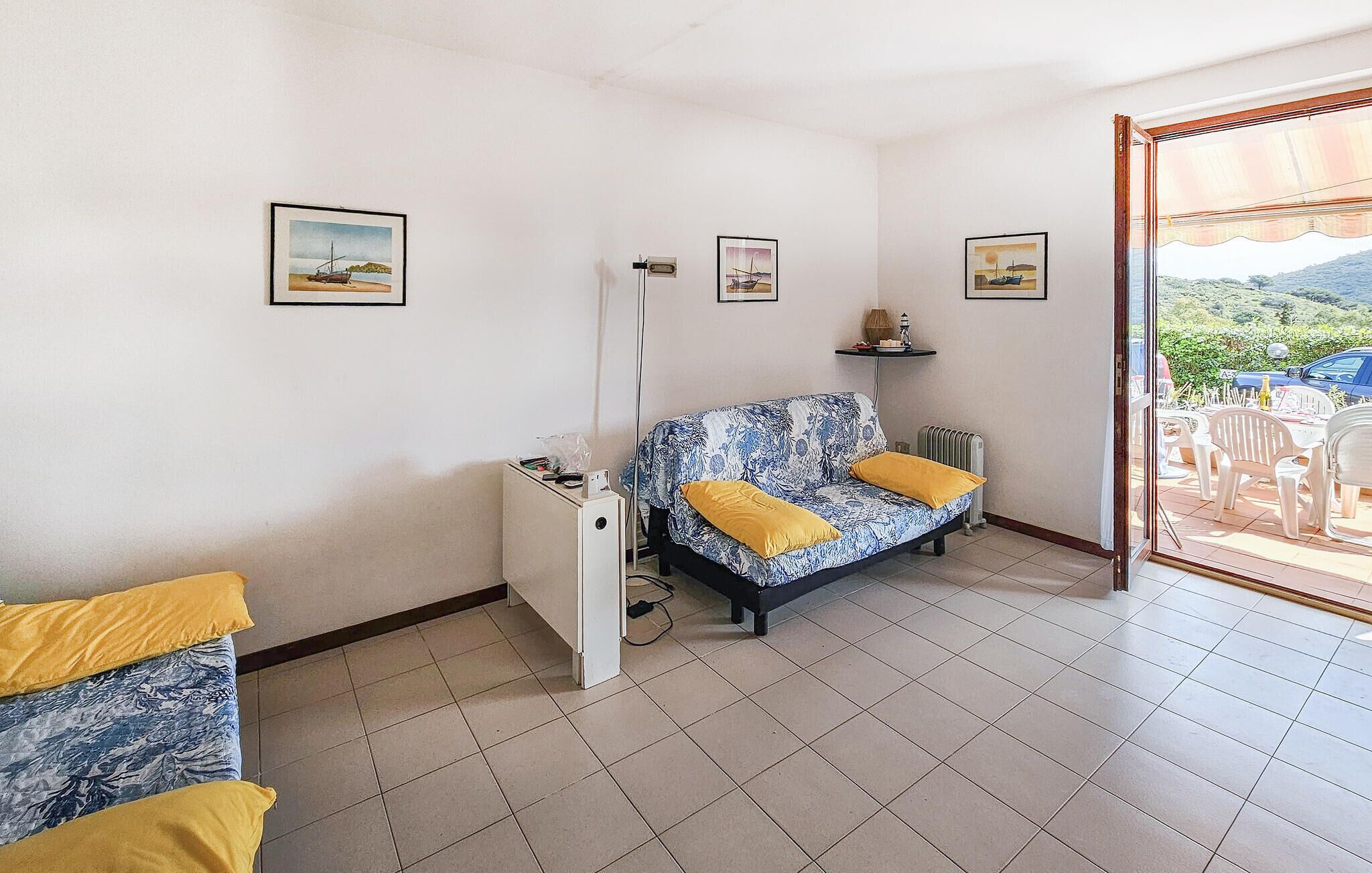 Een kamer met een slaapbank, een klein tafeltje en een radiator. Drie ingelijste foto's hangen aan de muur.