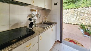 Een keuken met witte kastjes, een zwart aanrecht en een spoelbak. Er staan potplanten buiten.