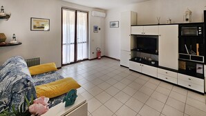 Een moderne woonkamer met een bank, een salontafel en een keukenhoek met kasten en apparatuur.