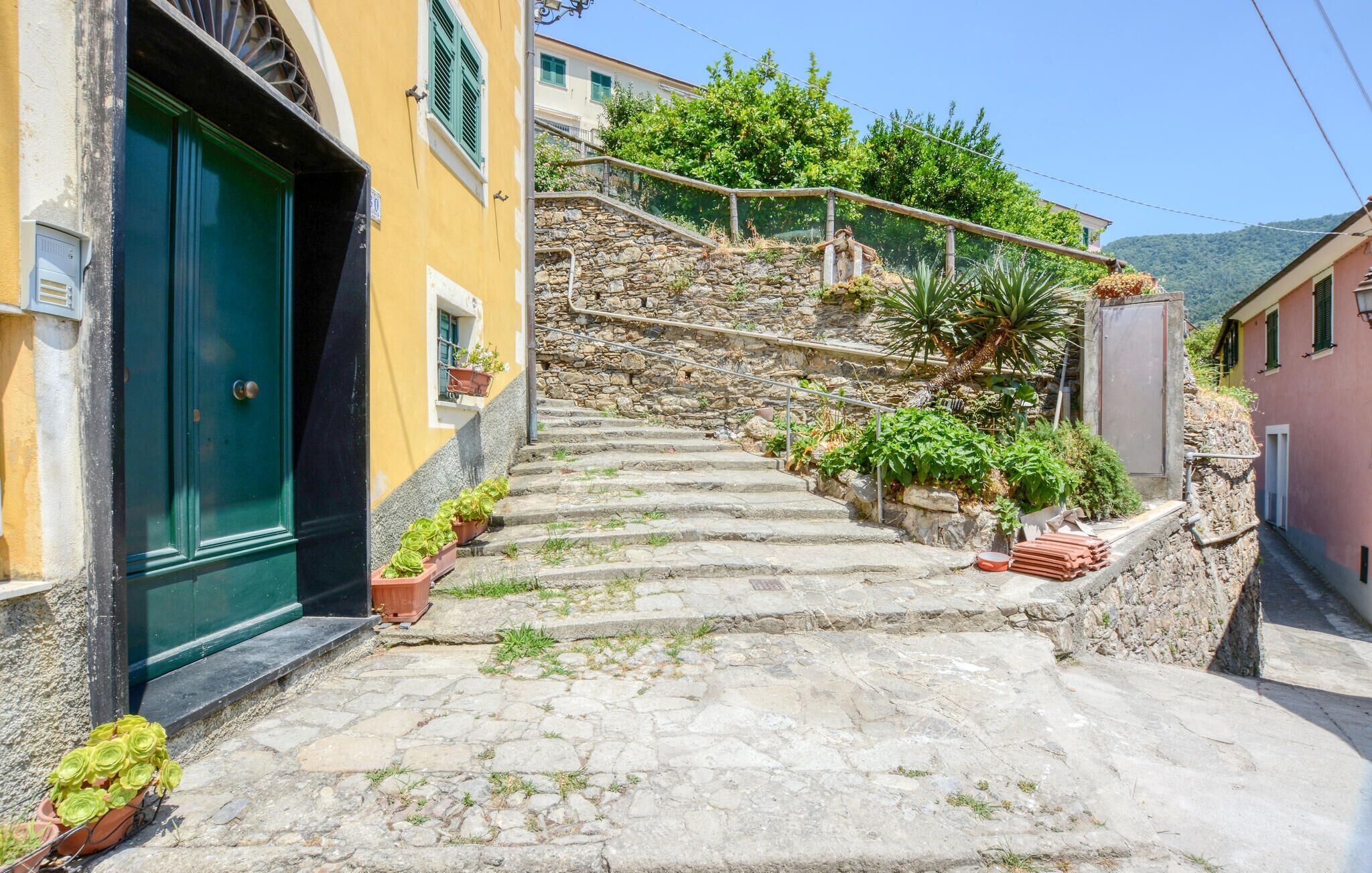 A narrow stone staircase leading up to a stone wall with greenery and a view of a mountain.