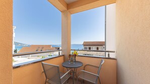 Een balkon met twee metalen stoelen en een kleine ronde tafel, met uitzicht op de kust, gebouwen en de zee.