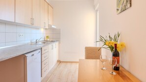 Een moderne keuken met lichte houten kastjes, een roestvrijstalen spoelbak en een houten eettafel met een fles wijn en twee glazen.